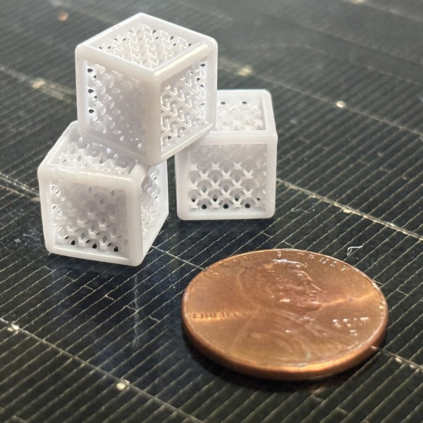 Miniature lattice-structure 3D prints shown next to a penny for scale
